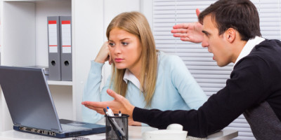 Bullying am Arbeitsplatz: Mann schreit Frau an, die vor dem Laptop sitzt