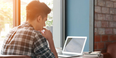Facebook-Freunde löschen ist Mobbing: junger Mann in Karo-Hemd sitzt vor dem Laptop