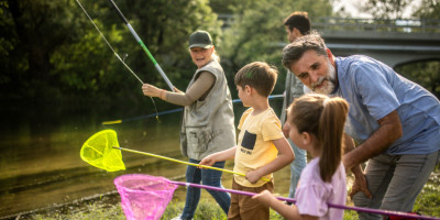 Eine Frau und zwei Männer stehen gemeinsam mit zwei Kindern an einem Fluss und angeln