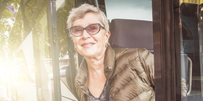 Ältere Frau schaut glücklich aus einem Bus heraus. 