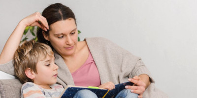 Unterhaltsvorschuss: Wer hat Anspruch darauf? Eine Mutter sitzt mit ihrem Sohn auf einer Couch und liest ein Buch.