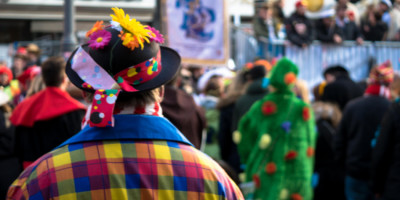 Verkleideter Mann mit buntem Hut und Shirt von hinten beim Karneval in einer Stadt