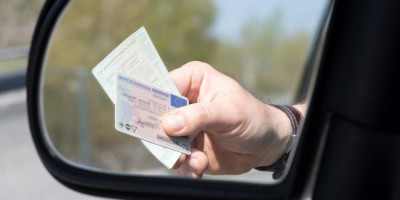 Hand im Rückspiegel zeigt Führerschein und Fahrzeugpapiere