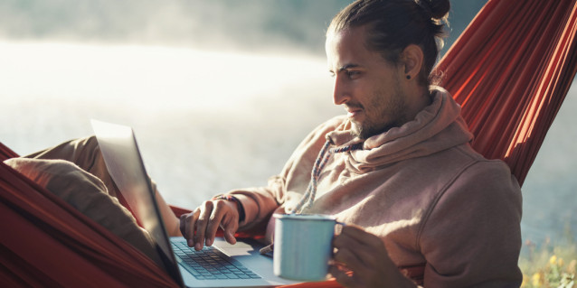 Arbeiten im Urlaub: Was ist erlaubt? Ein junger Mann sitzt mit Laptop in einer Hängematte