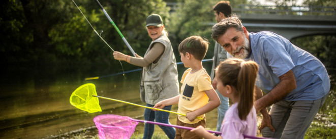 Eine Frau und zwei Männer stehen gemeinsam mit zwei Kindern an einem Fluss und angeln