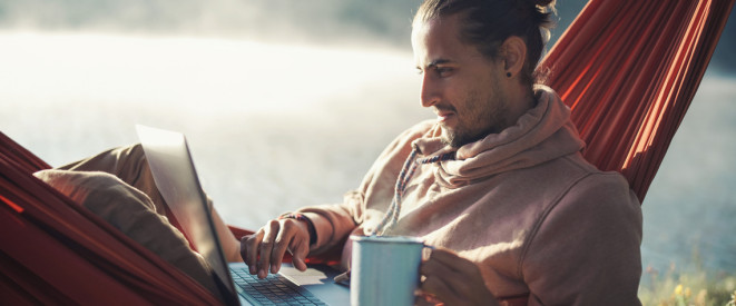 Arbeiten im Urlaub: Was ist erlaubt? Ein junger Mann sitzt mit Laptop in einer Hängematte