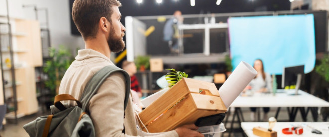 Mann verlässt mit gepacktem Rucksack und Kiste in der Hand ein Büro