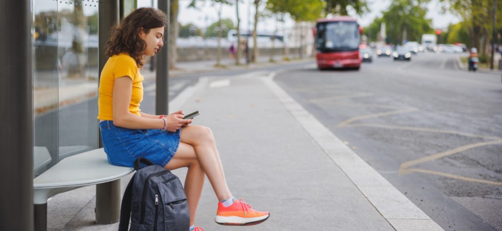 Female university student sitting and using phone while waiting for the bus to campus in the street in Paris, France