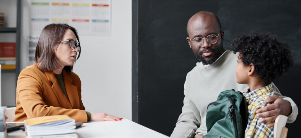 Young teacher talking to father of boy about his behavior while they sitting in classroom after lessons